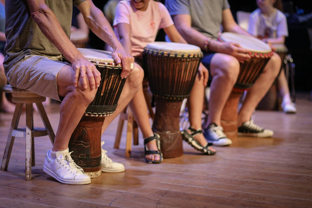 Une rangée de percussionnistes, petits et grands, djembé entre les genoux